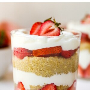 Strawberry, yogurt and quinoa parfaits, layered in a two glasses. A bowl of strawberries is behind the two parfaits.