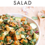 Bowl filled with roasted sweet potato salad with avocado and herbs. A wooden spoon is on the side. Text above reads "Roasted Sweet Potato Salad"