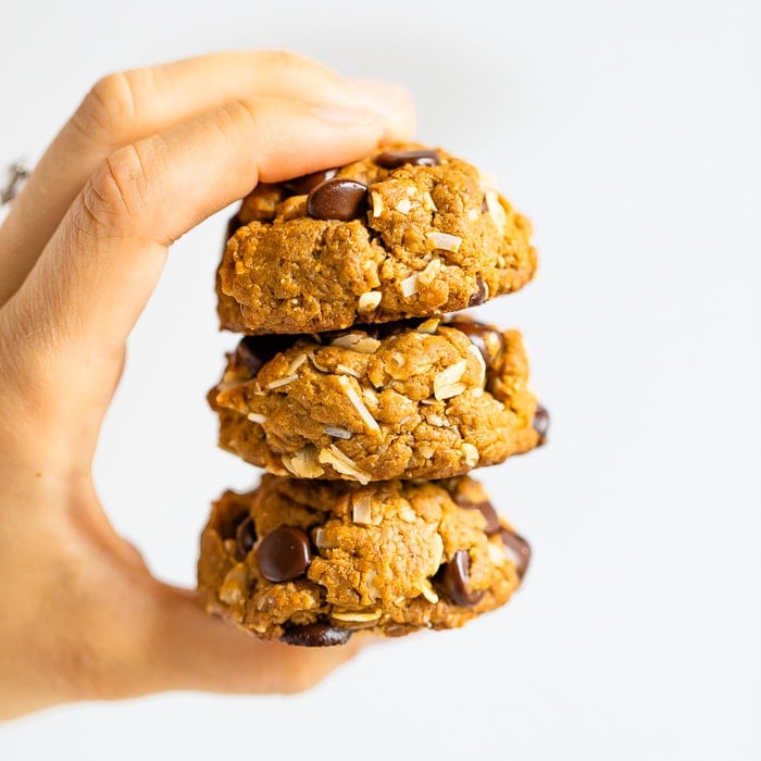 Hand holding a stack of three chocolate chip peanut butter oatmeal cookies with coconut.