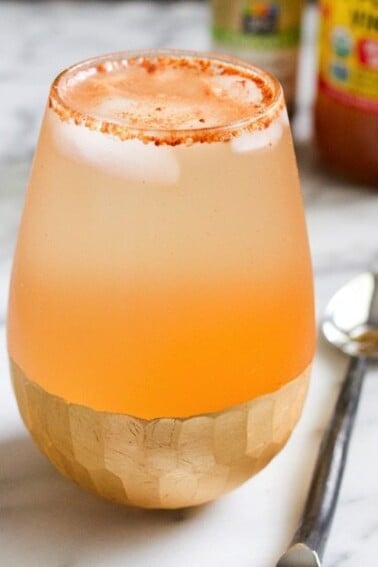 Apple Pie Apple Cider Vinegar Drink in clear shallow glass sitting on a marble countertop with a silver spoon next to it.