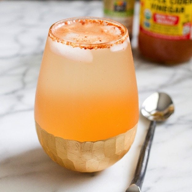 Apple Pie Apple Cider Vinegar Drink in clear shallow glass sitting on a marble countertop with a silver spoon next to it. 