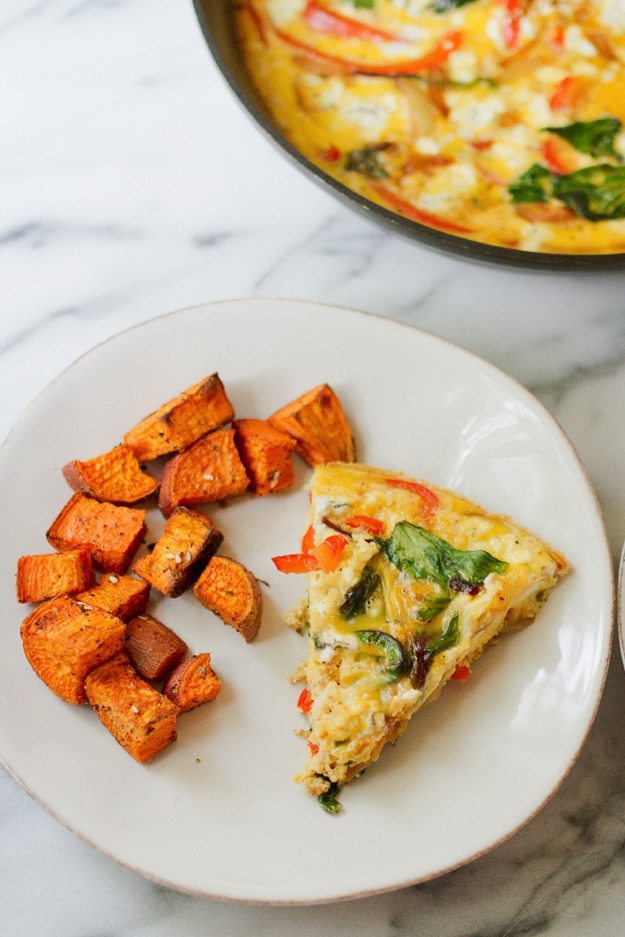 Caramelized Onion & Red Bell Pepper Frittata slice on a plate with roasted sweet potatoes.