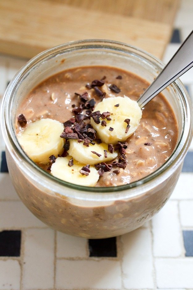 Overnight oats in a glass jar topped with cacao nibs and sliced bananas.