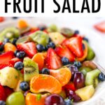 Bowl of fruit salad with strawberries, clementines, kiwi, grapes, blueberries and pineapple. Fruit salad is topped with lime zest.