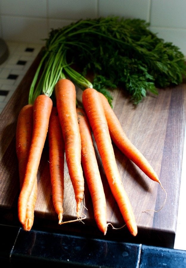 Fresh carrots with their greens still attached laying on a wooden cutting board.