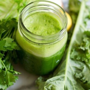 Green juice in a mason jar with foam on top. Kale and parsley are in the background.