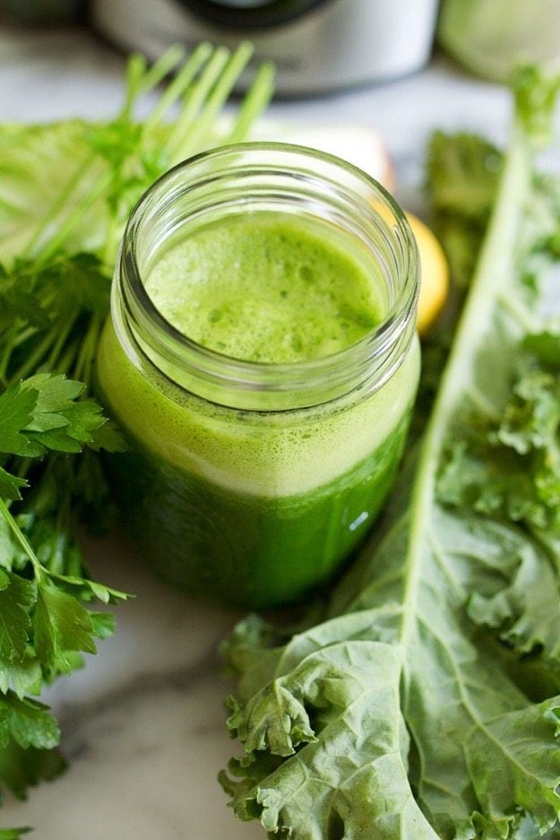 Green juice in a mason jar with foam on top. Kale and parsley are in the background. 