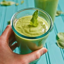 Pear smoothie with a sprig of mint on top, in a glass being held by a woman's hand.