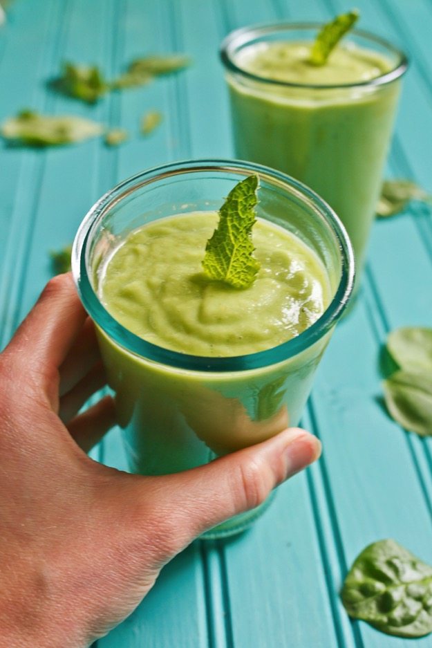 Pear smoothie with a sprig of mint on top, in a glass being held by a woman's hand. 
