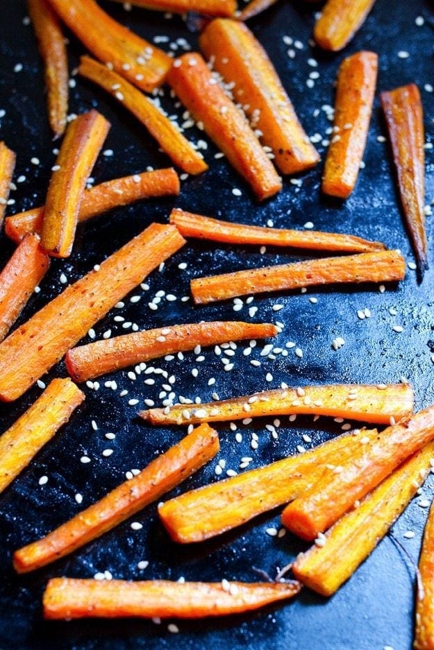 Sheet pan with slices of carrot sprinkled with sesame seeds.