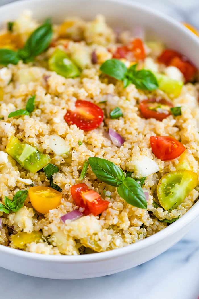 Bowl with Greek quinoa salad made with tomatoes, basil, red onion, feta, and quinoa.