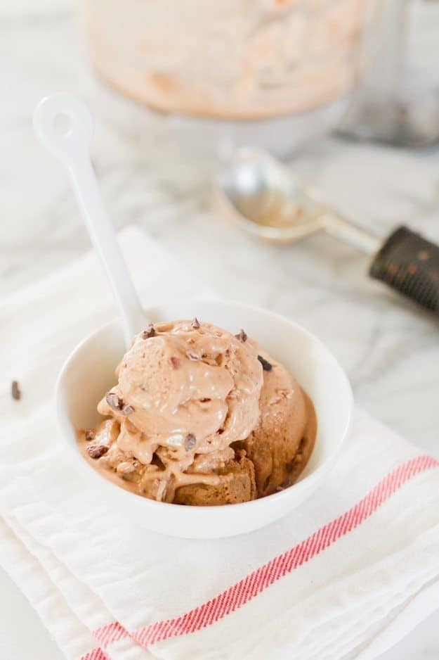 Chocolate banana nice cream in a bowl with a spoon. Ice cream scooper and food processor in the background.