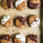 Cookie sheet lined with parchment paper. 9 no bake almond cookies half dipped in dark chocolate or white chocolate and sprinkled with cacao nibs.