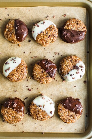 Cookie sheet lined with parchment paper. 9 no bake almond cookies half dipped in dark chocolate or white chocolate and sprinkled with cacao nibs.