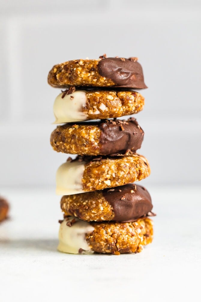 Stack of no bake almond cookies half dipped in either dark chocolate or white chocolate and sprinkled with cacao nibs.