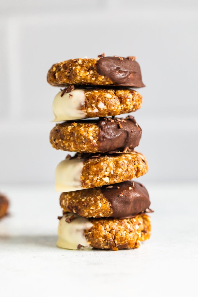 Stack of no bake almond cookies half dipped in either dark chocolate or white chocolate and sprinkled with cacao nibs.