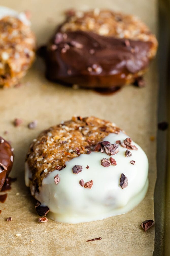 Close up photo of a no bake almond cookie dipped half way in white chocolate and sprinkled with cacao nibs.