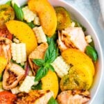 Salad topped with grilled salmon, corn, basil, peaches, and tomatoes.