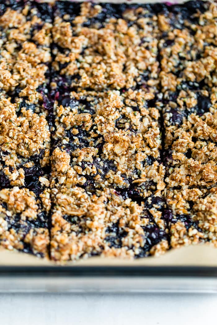 Close up of blueberry crumble bars sliced in a pan. The bars are topped with an oat and hemp crumble.