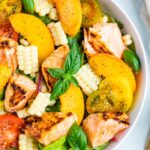 Salad topped with grilled salmon, corn, basil, peaches, and tomatoes.