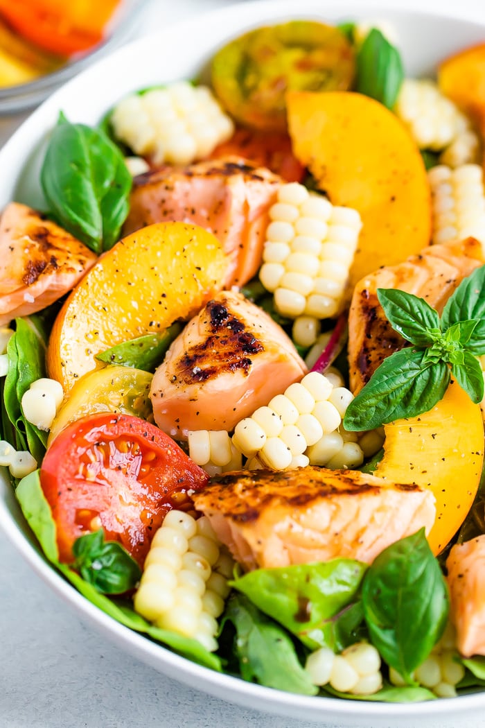 Salad topped with grilled salmon, corn, basil, peaches, and tomatoes.