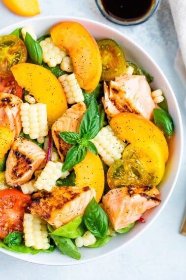 Salad topped with grilled salmon, corn, basil, peaches, and tomatoes.