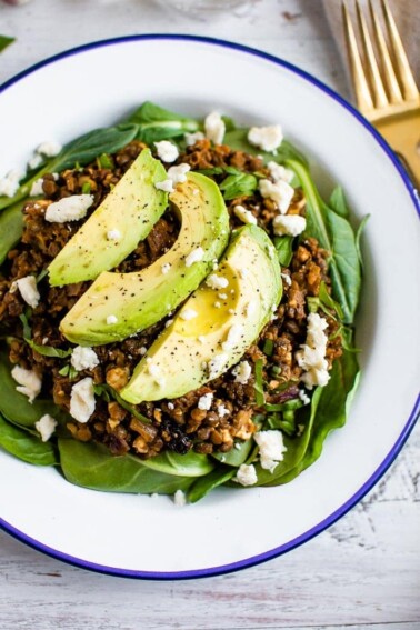 Plate with a bed of fresh spinach topped with a warm Mediterranean salad, topped with feta and avocado.