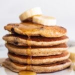 Stack of banana chocolate chip pancakes topped with banana slices and maple syrup.