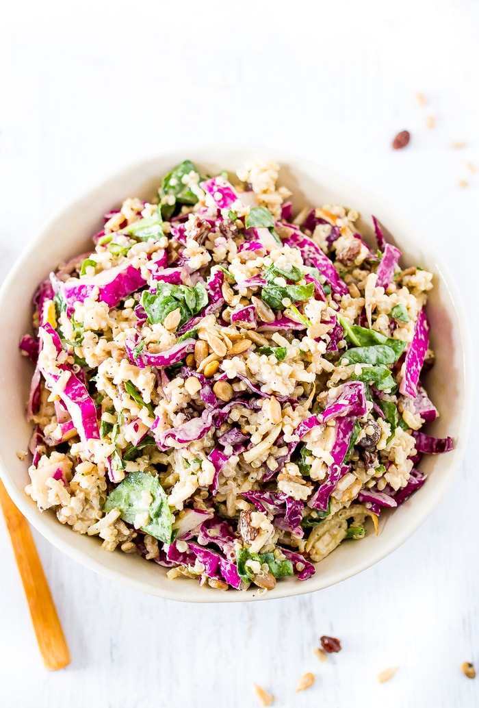 Bowl of spiralized apple slaw, filled with apples, spinach, quinoa and cabbage. The corner of the fork to the side.