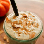 Creamy coconut pumpkin chia pudding in a glass with a spoon and topped with coconut and almond butter. A mini pumpkin is off to the side.