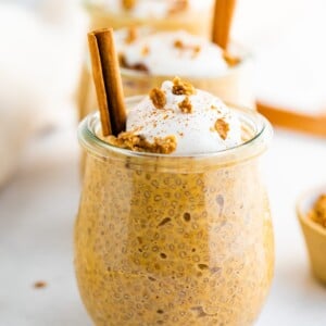 Pumpkin chia pudding in a tulip weck jar, topped with coconut whipped cream, granola and a cinnamon stick.