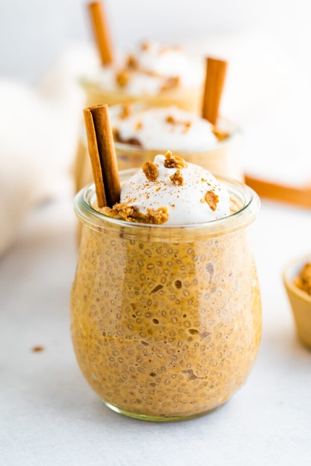 Pumpkin chia pudding in a tulip weck jar, topped with coconut whipped cream, granola and a cinnamon stick.