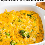 Baking dish with cheesy broccoli quinoa casserole. A wood spoon and dish towel are around the dish.