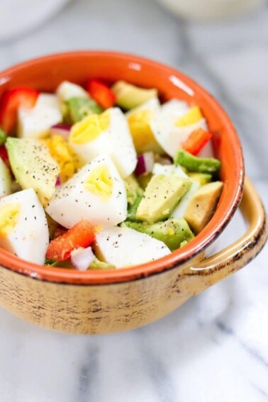 Chopped hard boiled egg and avocado with chopped peppers and onions in a bowl.