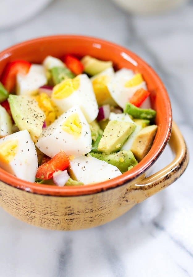 Chopped hard boiled eggs and chopped avocado with vegetables in a bowl. 