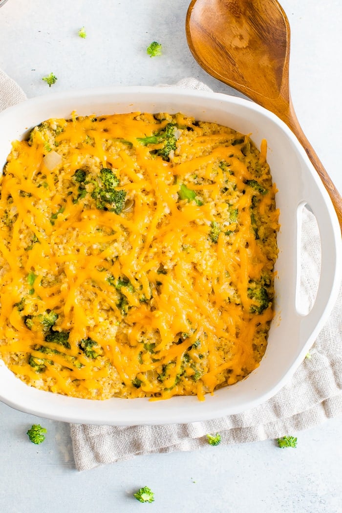 Baking dish with cheesy broccoli quinoa casserole. A wood spoon and dish towel are around the dish.