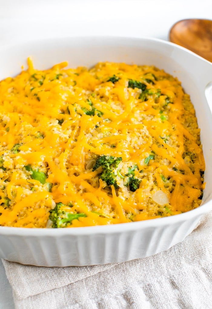 Baking dish with cheesy broccoli quinoa casserole. A wood spoon and dish towel are around the dish.