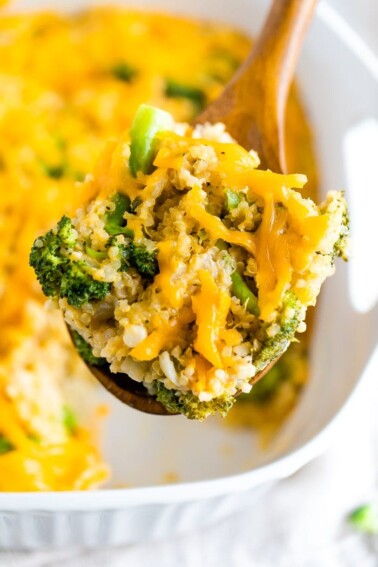 Broccoli quinoa casserole with cheddar cheese on a large wooden spoon.