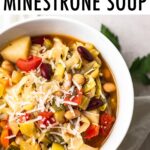A white bowl with minestrone soup. A loaf of bread is in the background.