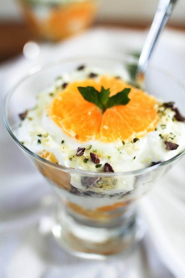 Close up of a clementine slice on top of the greek yogurt parfait in a glass bowl.