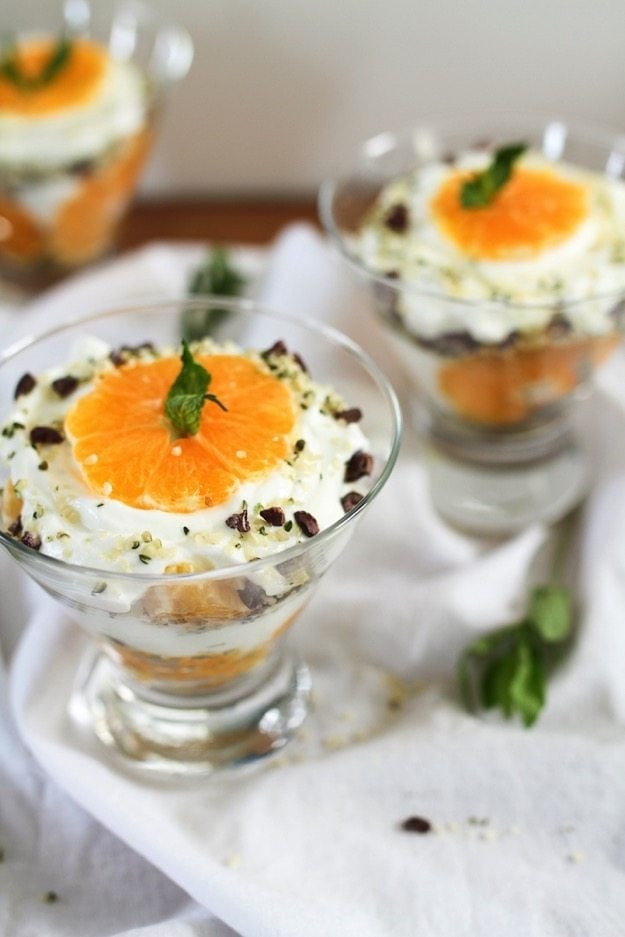 A glass bowl of clementine greek yogurt parfait on a white table cloth.