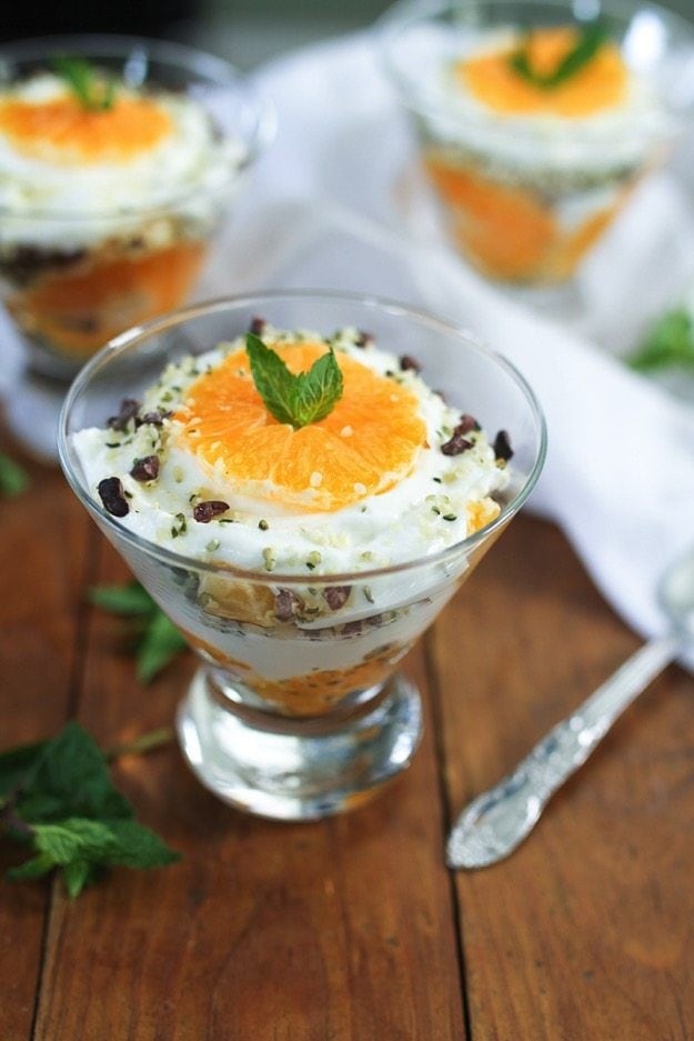 Glass bowl of clementine greek yogurt parfait with two other bowls in the background.