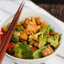 Kung Pao Tempeh in a bowl with stir fried veggies and chop sticks.