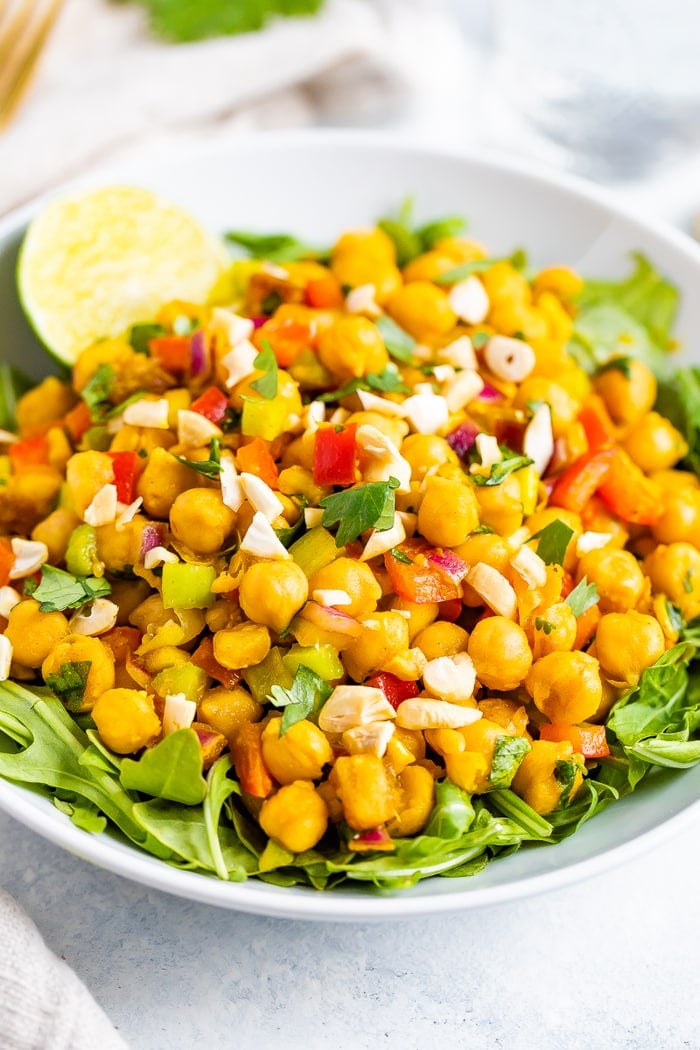 Bowl of curried chickpea salad made with chopped red onion, red pepper, cilantro, and dates, served over a bed of greens.