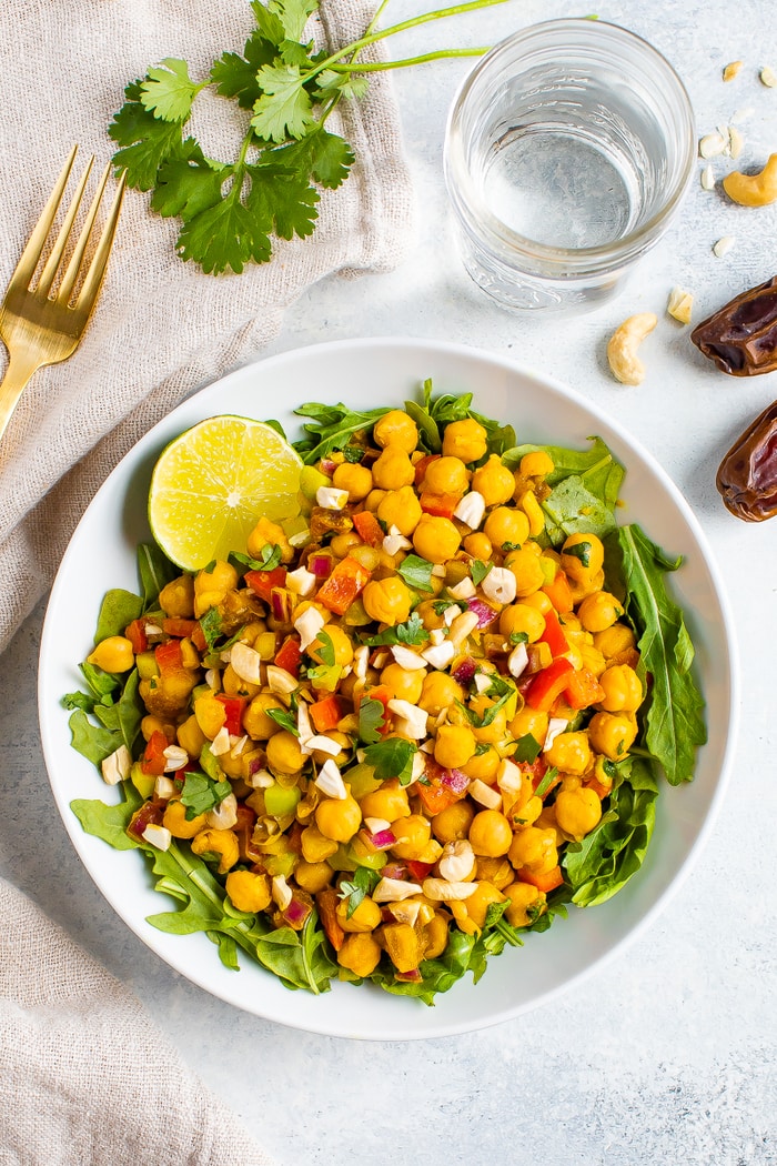 Bowl of curried chickpea salad made with chopped red onion, red pepper, cilantro, and dates, served over a bed of greens.