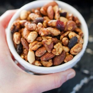 Hand holding a white bowl with cajun spiced trail mix, full of nuts, seeds, and raisins.