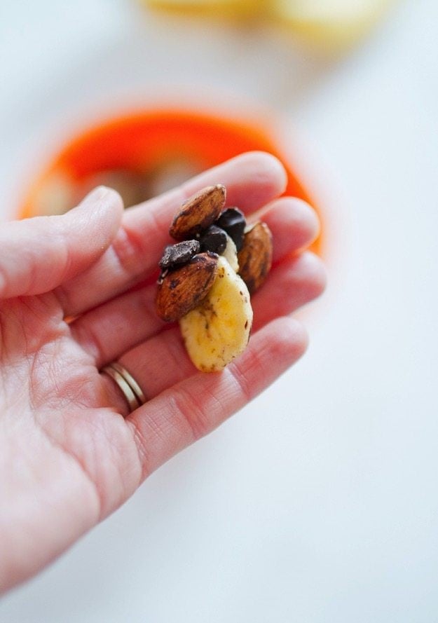 Hand holding trail mix with banana chips, chocolate and almonds.