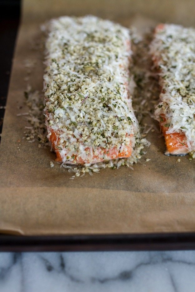 Salmon covered with a hemp and pecorino coating on a sheet pan lined with brown parchment paper.