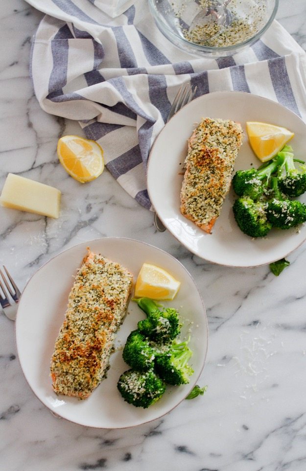 An overhead photo of two plates with hemp and pecorino crusted salmon served with a side of broccoli and a lemon wedge.