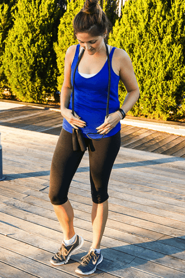 Girl in black workout pants and blue tank top holding a black jump rope outside.